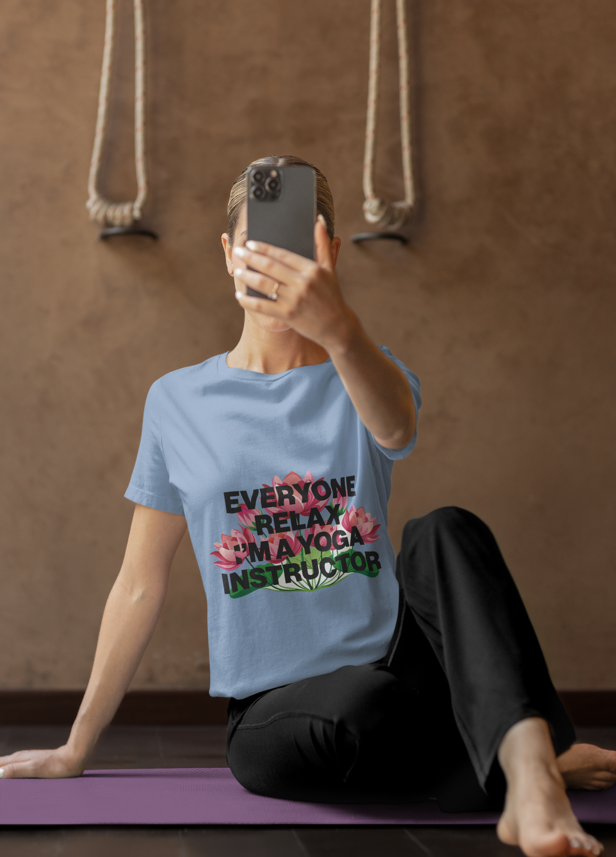 Person sitting on a yoga mat wearing a t-shirt with a humorous yoga instructor message.