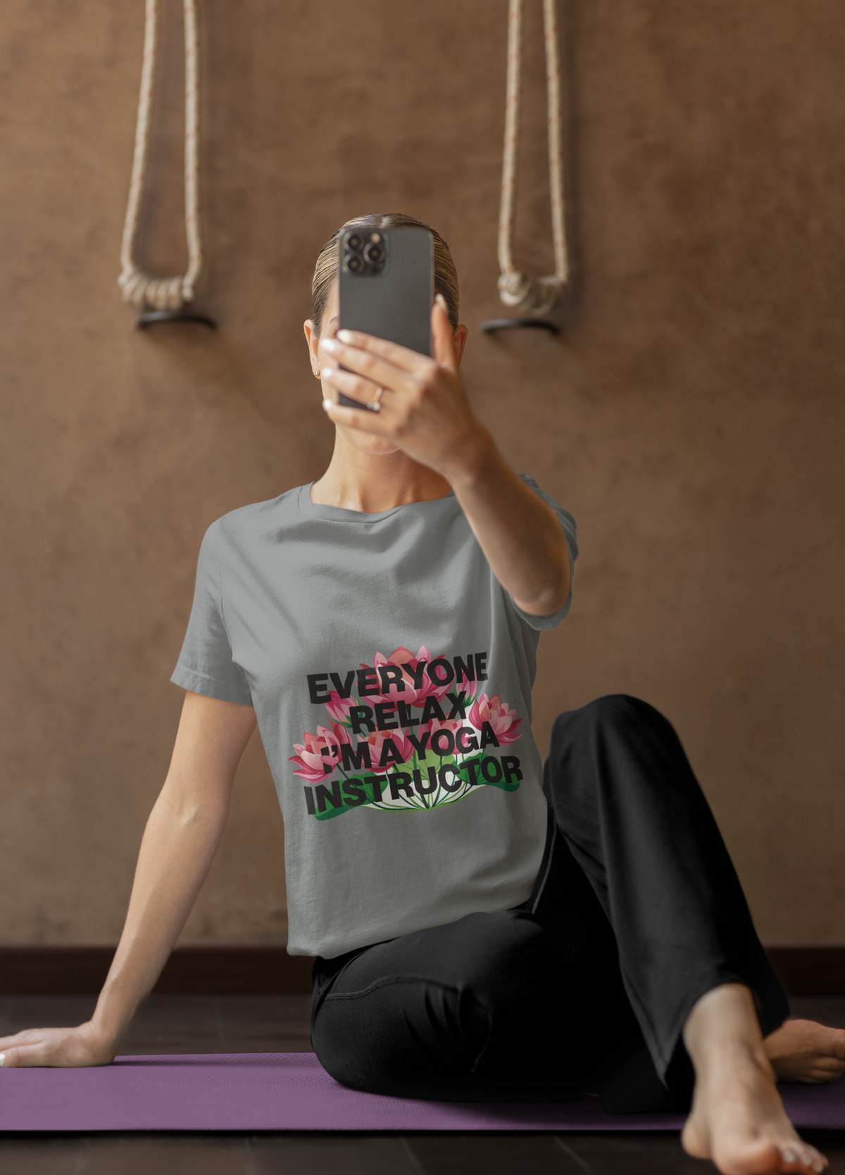 Person sitting on a yoga mat wearing a t-shirt with text and flower graphics.