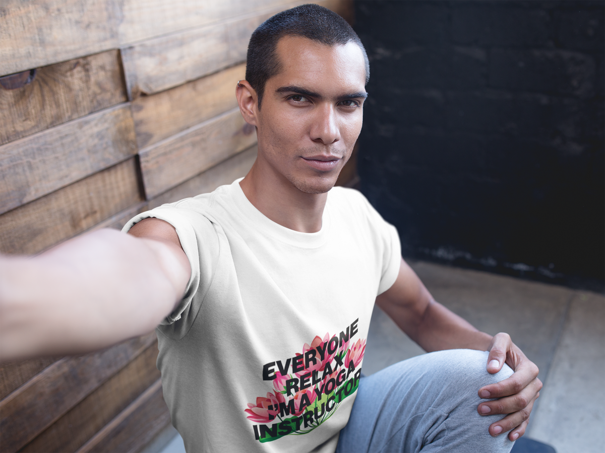 Man wearing a white t-shirt with colorful text and graphics, sitting against a wooden wall.