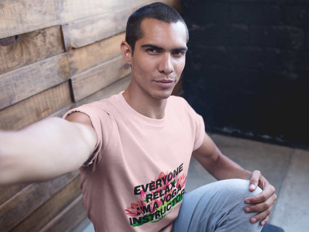 Man wearing a pink t-shirt with text, sitting against a wooden wall.