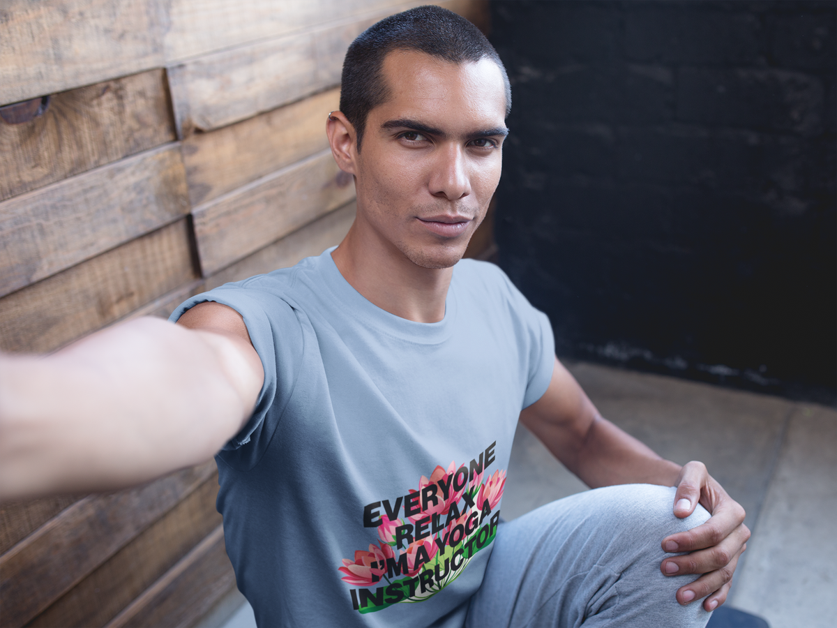 Man wearing a t-shirt with text and graphics, sitting against a wooden wall.